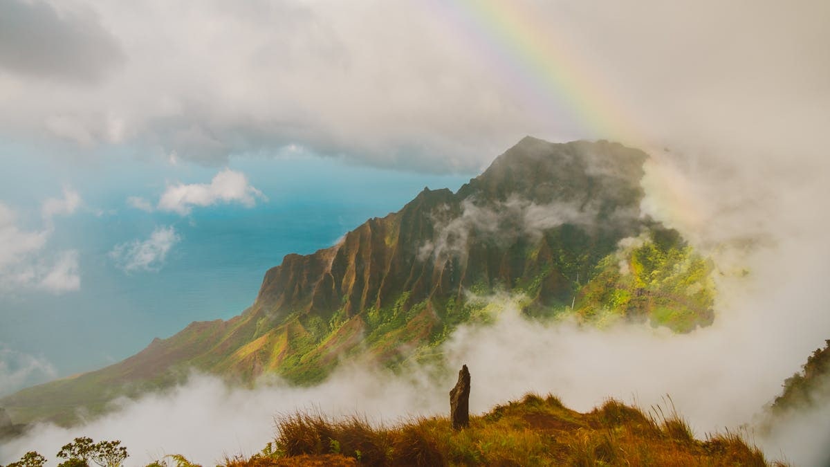 Stunning landscape of Hawaiian cliffs with a rainbow and misty clouds.